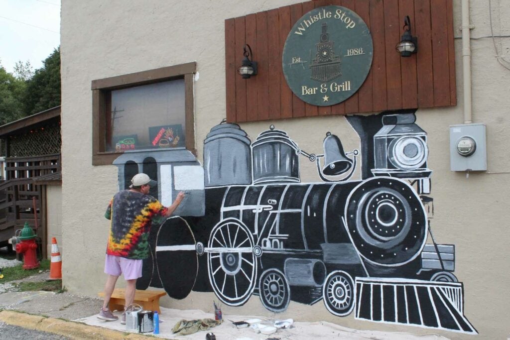 Artist Sheri Gaudet works on a new mural on the side of the Whistle Stop.