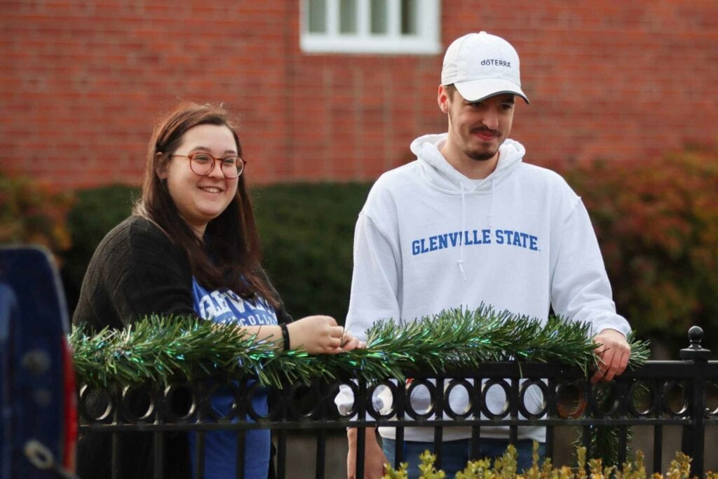 Glenville State College Student Life Program Assistant Hannah Rexroad and Student Government Association President Nic McVaney string garland along the fence at Glenville’s City Square Park.